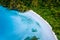 Aerial top down view of boat moored at secluded white sand beach with coconut palm trees and surreal turquoise blue