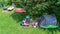 Aerial top view of campsite from above, mother and daughter having fun, tent and camping equipment under tree, family vacation