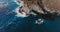 Aerial top view drone shot of beautiful blue ocean waves crashing over sunny rocky coast line in Big Sur California.