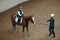 Aerial, top view. Female teacher, instructor teaching little girl, kid horseback riding. Outdoor lesson