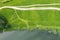 Aerial top view of green meadow on lakeside and dirt road