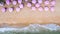 Aerial top view on the sandy beach. Pink umbrellas, sand, beach chairs and sea waves