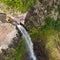Aerial top view of travel couple waving to drone, standing on the edge of 500 feet waterfall in the tropical island