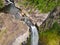 Aerial top view of travel couple waving to drone, standing on the edge of 500 feet waterfall in the tropical island