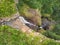 Aerial top view of travel couple waving to drone, standing on the edge of 500 feet waterfall in the tropical island