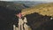 Aerial tourist woman rise hands. Girl sit on stone at mountain top. Nature landscape. Mount rock