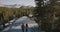 Aerial tracking shot of young newlyweds hiking together on amazing white rock towards epic Yosemite park forest skyline.