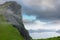 AERIAL: Unrecognizable woman hiking down a grassy mountain overlooking the ocean