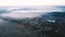 Aerial video footage. Foggy cold morning countryside. Small rich village surrounded by misty valley and fields. Road