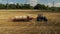 Aerial video. Rolling haystacks in countryside on the field on a cloudy day. Tractor loading hay bales on truck trailer