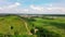 Aerial view from above on the country road in mountain range in between green grass and trees around