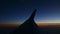 Aerial view from aircraft window across steel wing silhouette at dark sunset sky