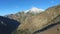 Aerial view along the side of a mountain with views of the snowcapped mountain top and the steep valley below