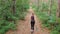 Aerial view from the back to the young woman who runs along the path in a pine thick forest