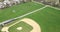 Aerial view of a baseball and soccer field in a large suburban park with a sports field mower tractor grooming the grass