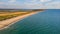 An aerial view of a beautiful sandy beach along blue water sea and amaizing cliffs in the background at golden hour under a