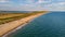 An aerial view of a beautiful sandy beach along blue water sea and amaizing cliffs in the background at golden hour under a