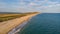 An aerial view of a beautiful sandy beach along blue water sea and amaizing cliffs in the background at golden hour under a