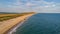 An aerial view of a beautiful sandy beach along blue water sea and amaizing cliffs in the background at golden hour under a