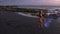 Aerial view of beautiful sensual woman in bikini dancing with colored smoke at the black sand beach during sunset