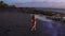 Aerial view of beautiful sensual woman in bikini dancing with colored smoke at the black sand beach during sunset