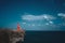 Aerial view of beautiful woman in red dress on the sea shore cliff during sunny summer day