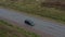 Aerial view of black car moves on road with beautiful landscape between fields. Top view. Shooting from a drone or