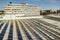 Aerial view of blue shiny solar photo voltaic panels system on commercial roof producing renewable clean energy on city landscape