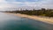 An aerial view of the Boscombe Beach with sandy beach, calm flat water, groynes breakwaters, grassy cliff and building in the