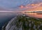 Aerial view of a building at the edge of a rocky coast at a mesmerizing pink sunset