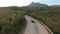 Aerial view of a car driving along agriculture field and green forested valley. Shot. A passenger car following