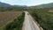 Aerial view of a car driving along agriculture field and green forested valley. Shot. A passenger car following