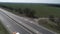 Aerial view of car driving along the empty gravel road through green meadows landscape on sunny morning. Drone chasing a car.