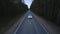 Aerial view car driving on dark countryside road among summer forest at evening