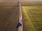 Aerial view of car driving by straight ground road through green fields on sunny blue sky copy space background. Drone photography