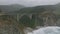 Aerial view of cars passing over Bixby Creek Bridge on Big Sur coast. High concrete bridge with big arch. Waves the