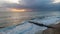 An aerial view of a choppy sea with crashing waves, groynes breakwater and sandy beach under a stormy cloudy grey sky with ray