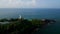 Aerial view of coastal lighthouse on cliff. Waves crash against rocks. Timeless navigation landmark with greenery. Ocean