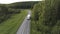 Aerial view of the concrete road and green grass and trees growing along it, white wagon with goods moving on the empty