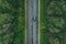 Aerial view of country road with car driving through green forest and corn fields