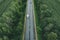 Aerial view of country road with car driving through green forest and corn fields