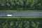 Aerial view of country road with car driving through green forest and corn fields