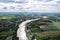 Aerial view of curved large river and village living by the water and agricultural field in countryside at suburban