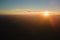 Aerial view of dark mountain hills with bright sunrays of setting sun at sunset. Hazy peaks and misty valleys in evening