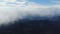 Aerial view. Dense white mist covers forested mountains. Blue autumn sky.