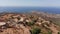 Aerial view of desert rocky small city on the top of mountain hill. In the background coastline with modern city. Aerial