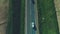 Aerial view of different type cars driving along the empty gravel road through green meadows and agriculture fields
