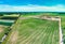 Aerial view from a distance onto a gravel pit with a large ploughed field in the foreground covered with young green plants,