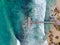 Aerial view of dock over tropical blue water and sand beach, with waves.