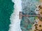 Aerial view of dock over tropical blue water and sand beach, with waves.